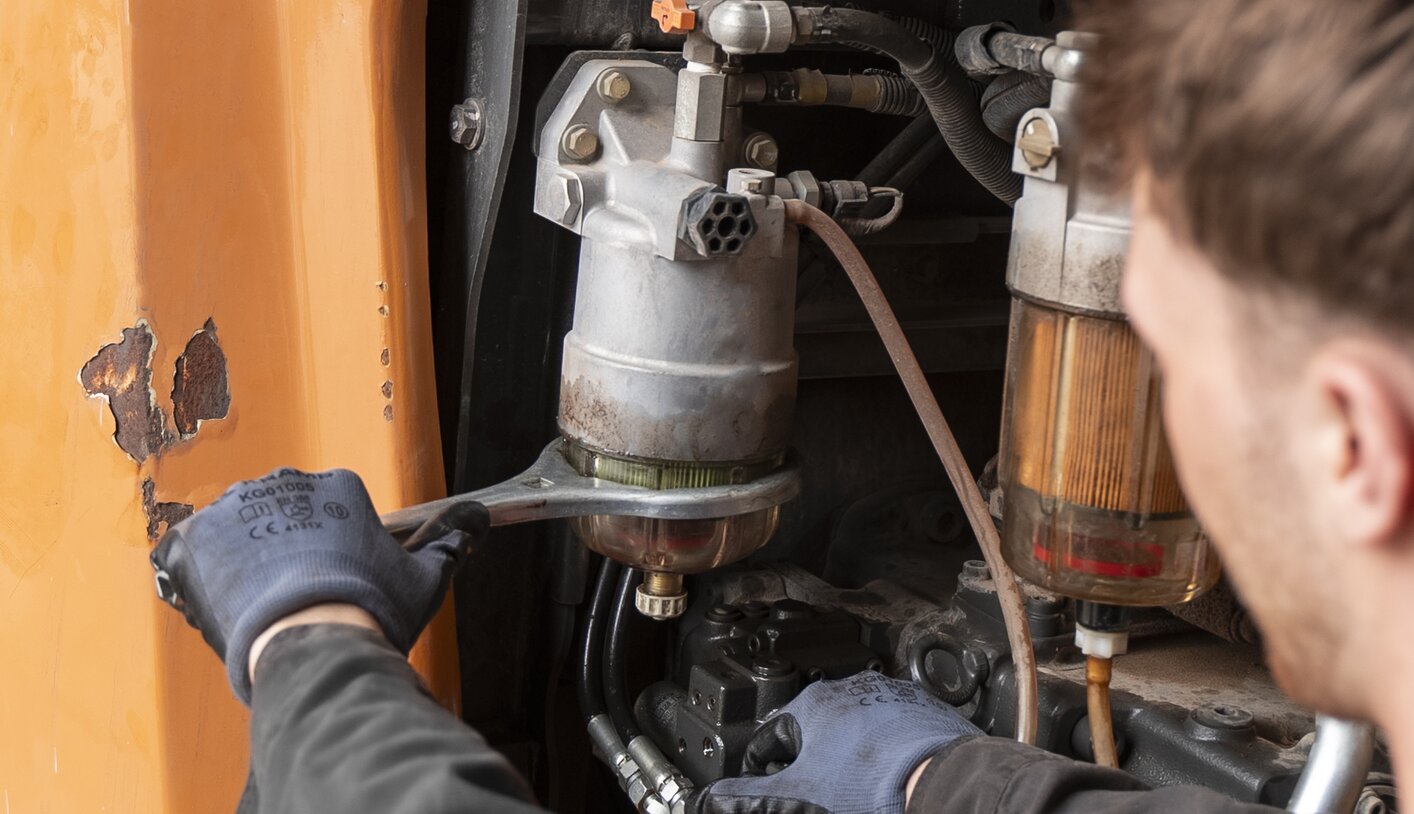 A mechanic is repairing a Case excavator, focused on the engine area.